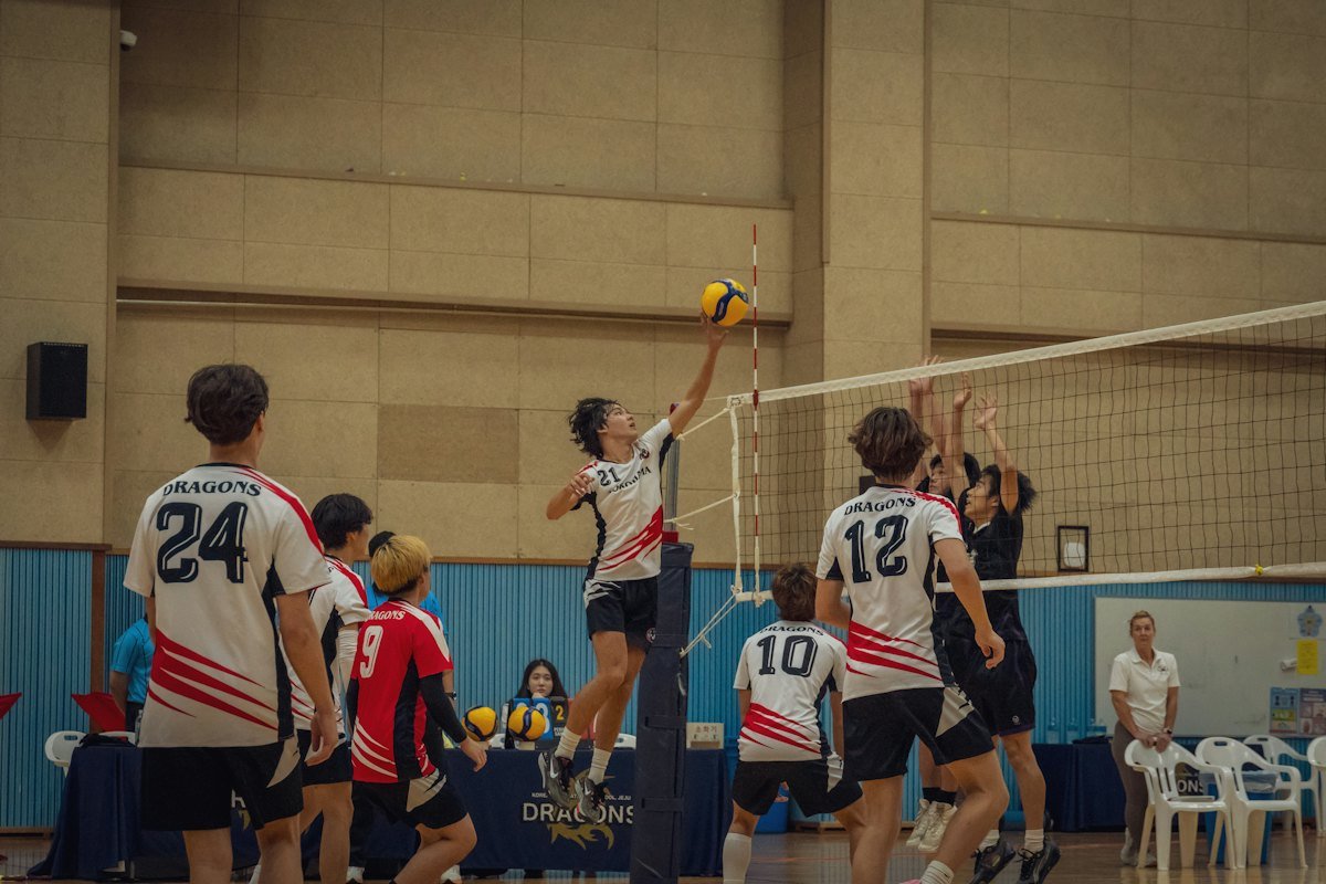 An indoor match, players spread across the court as the ball comes over the net